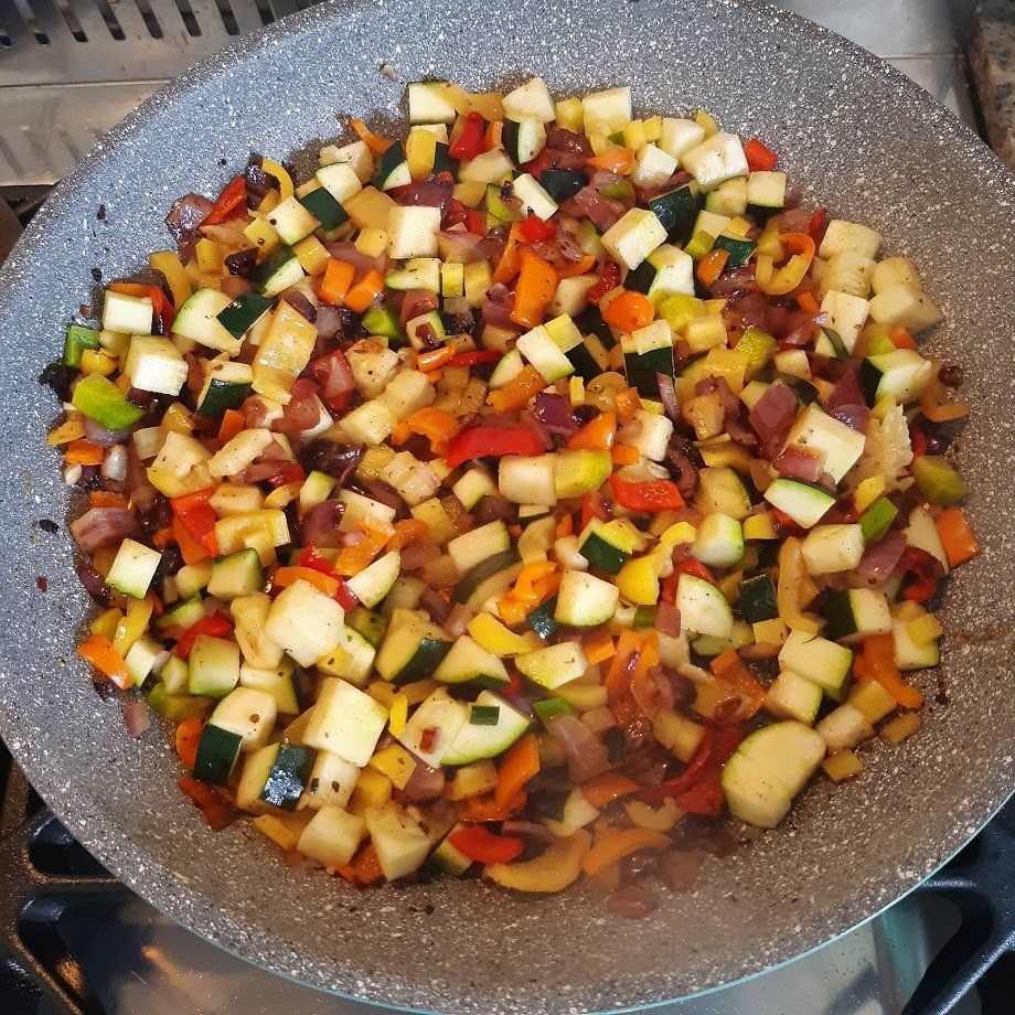 In blokjes gesneden groenten (courgette, paprika, uien) worden in een pan op het fornuis gebakken.