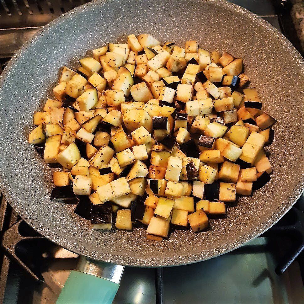 In blokjes gesneden aubergine wordt gebakken in een grijze koekenpan op het fornuis.