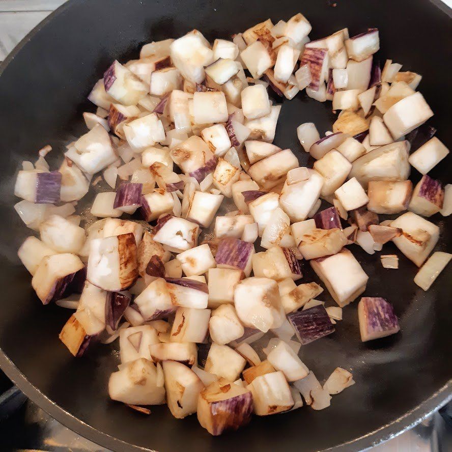 In blokjes gesneden aubergine en ui worden in een pan gebakken; sommige stukjes worden bruin.