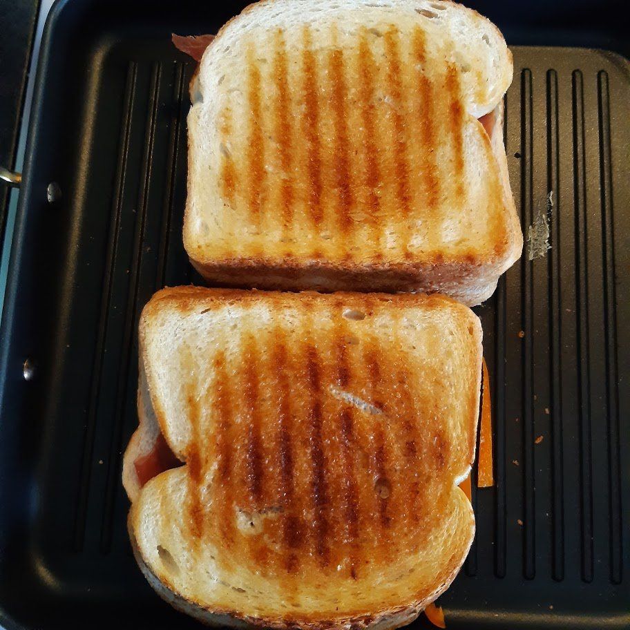 Twee geroosterde sandwiches op een grillpan, met duidelijke grillstrepen.