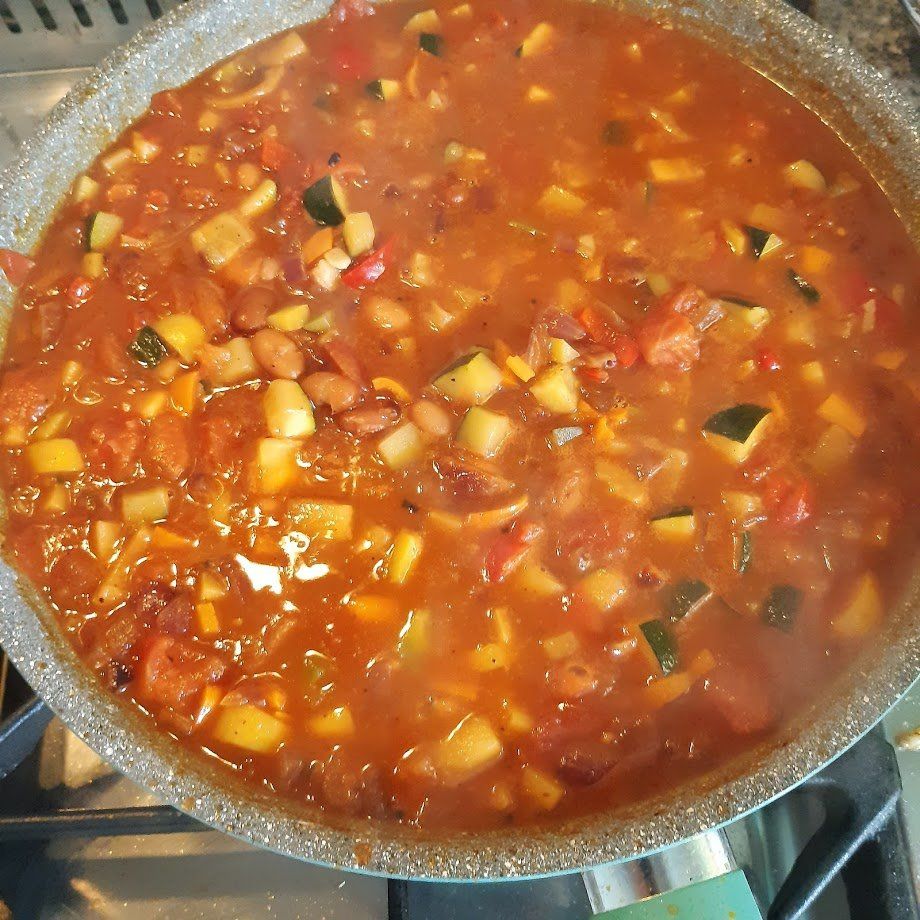 Een pan met sudderende groentesoep op basis van tomaten, met courgette, wortelen en bonen.