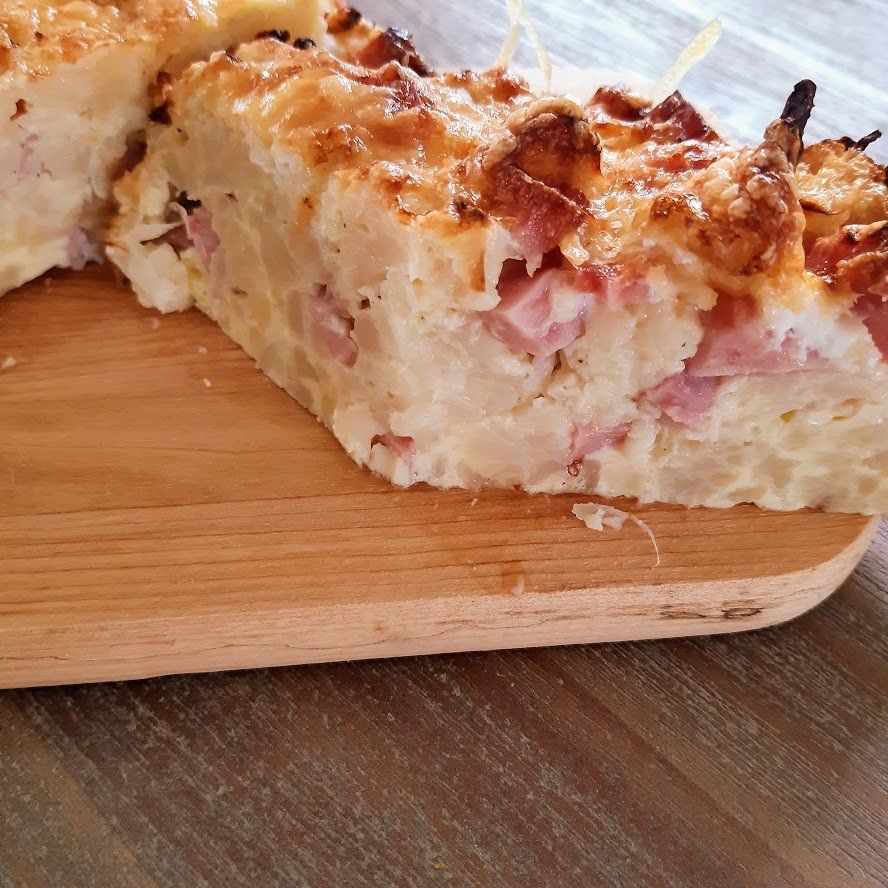 Ovenschotel met pasta, ham en een goudbruine korst, geserveerd op een houten plank.