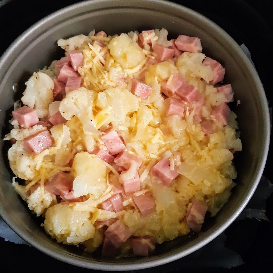 Bloemkool- en hamschotel met geraspte kaas in een ronde ovenschaal.