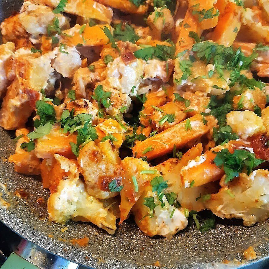Een pan met gekookte kip, zoete aardappelen en bloemkool, gegarneerd met peterselie.