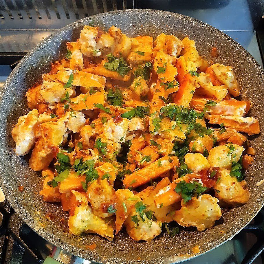 Een pan met geroosterde groenten, waaronder wortels, bloemkool en kruiden, die op het fornuis staat te koken.