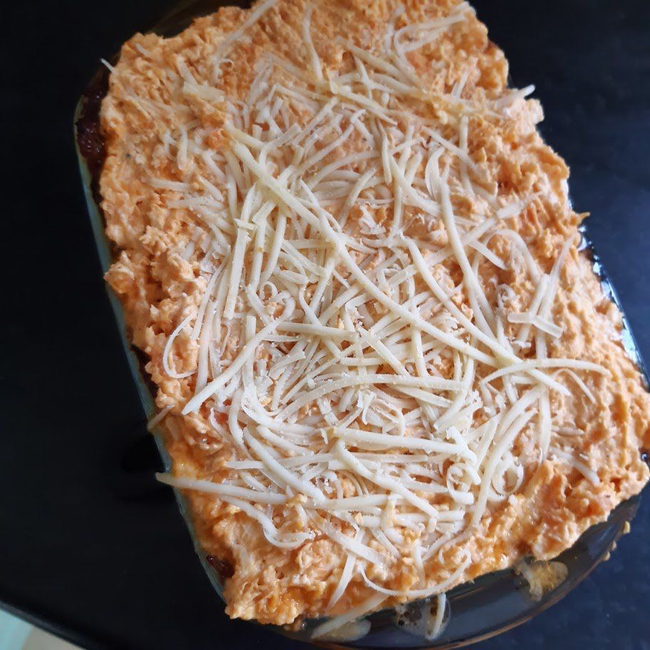 Glazen ovenschaal met een romige, roodachtige topping en geraspte kaas.