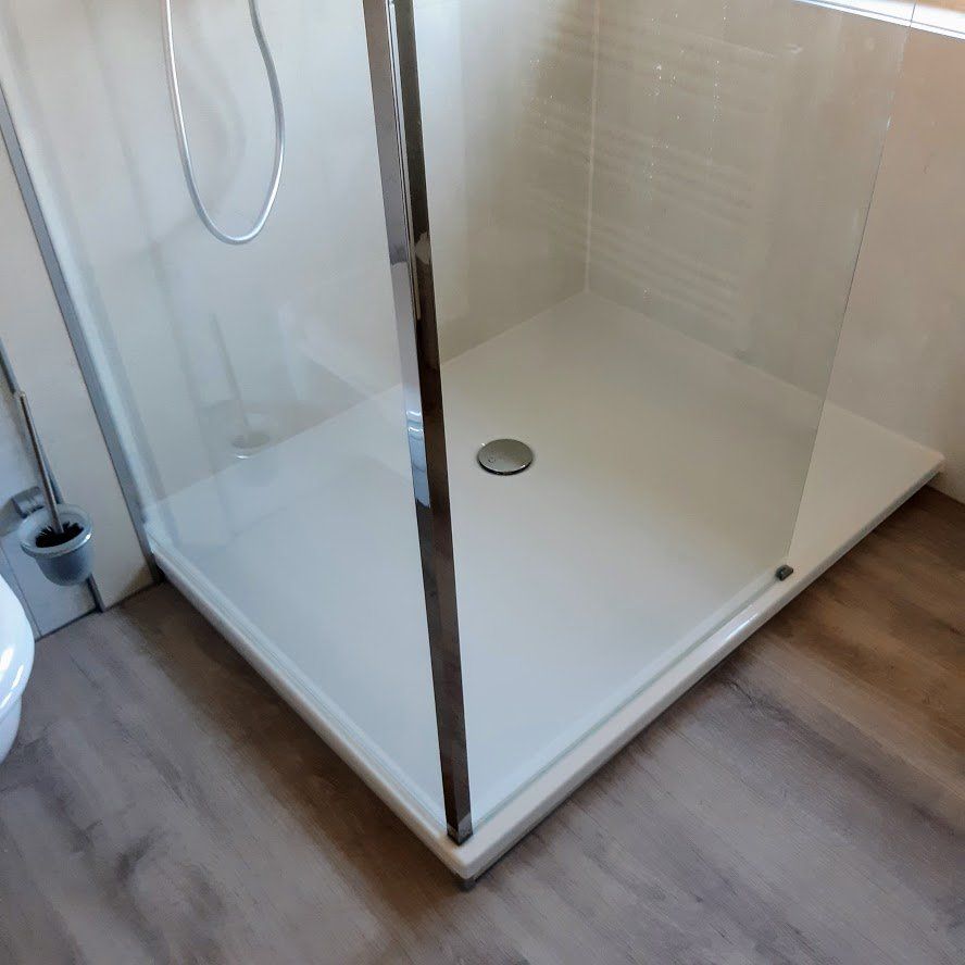 Een witte hoekdouche met een glazen deur, chromen kranen en een afvoer.