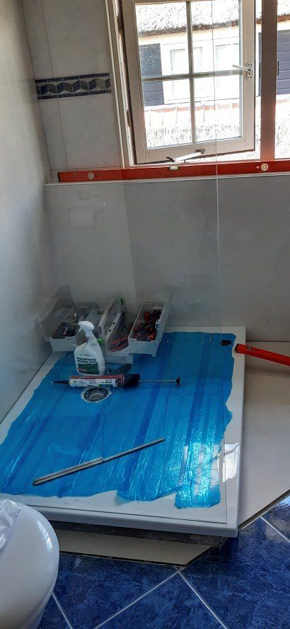 Een douchecabine met een beschermende blauwe folie. Gereedschap en schoonmaakspullen liggen op de bodem. Op de achtergrond is een raam te zien.