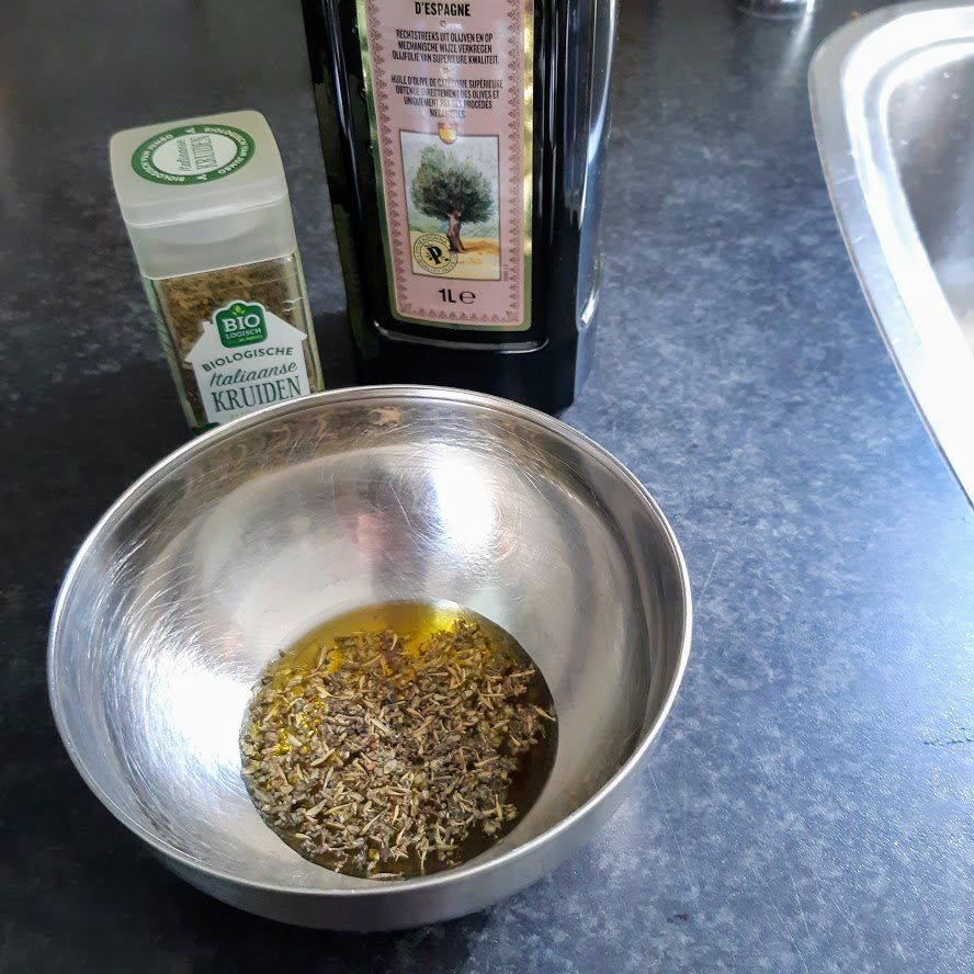 Een kom met olijfolie en kruiden, een fles olijfolie en een kruidenpotje op een donker aanrecht.