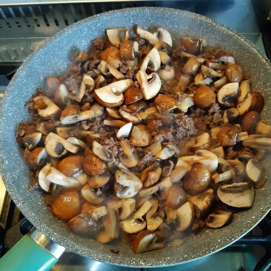 Champignons en gehakt worden in een grijze pan op het fornuis gebakken.