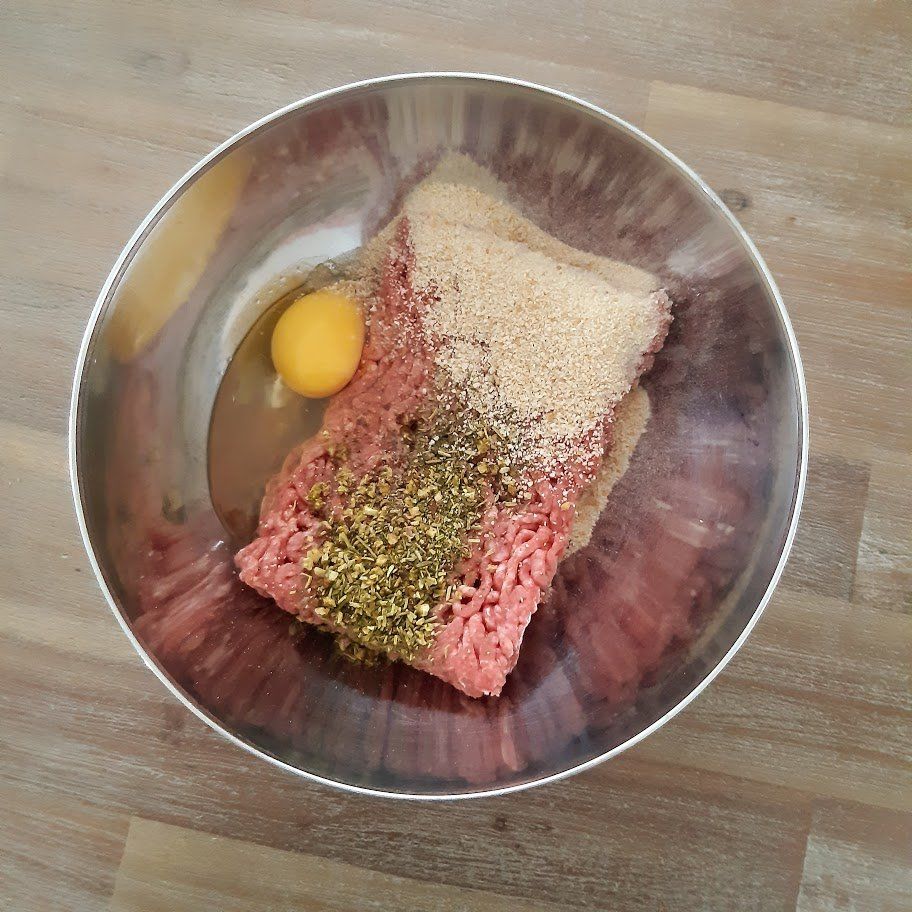 Doe het gehakt, het ei en de kruiden in een metalen mengkom, klaar om te worden gemengd.
