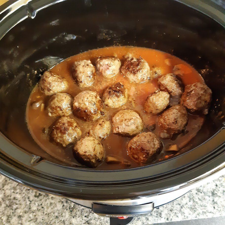 Gehaktballetjes sudderen in een donkere saus in een zwarte slowcooker.