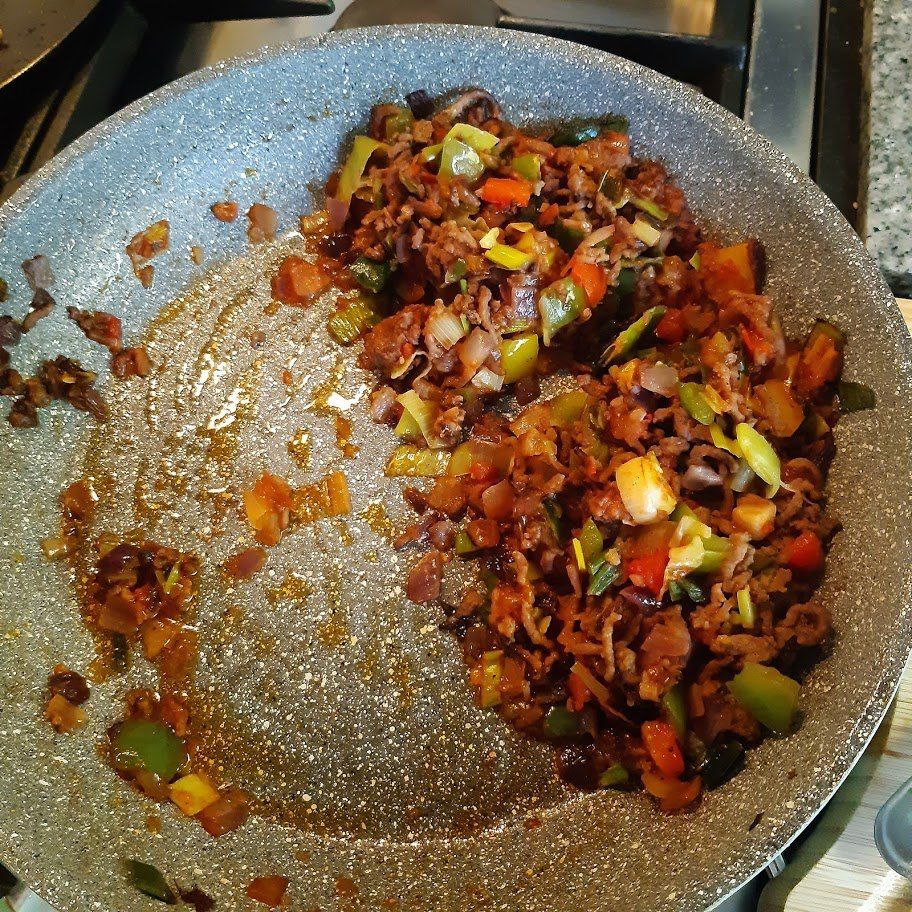 Gebakken groenten en vlees in een grijze pan op het fornuis. Groene, rode en bruine ingrediënten.