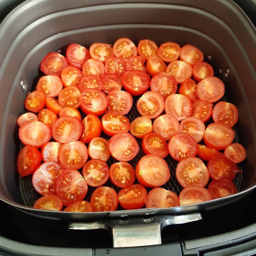 Gehalveerde tomaten in een mandje van de airfryer, klaar om te bereiden.