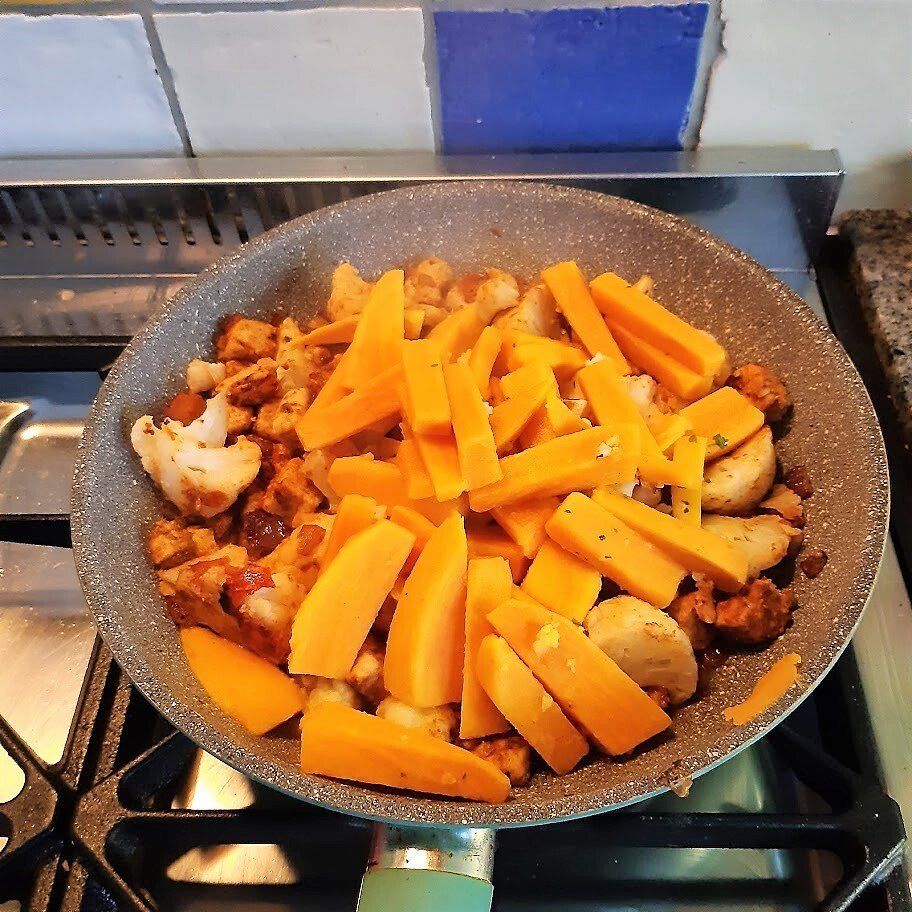 Groenten die in een pan op het fornuis worden gekookt, met oranje wortelstaafjes en andere ingrediënten.