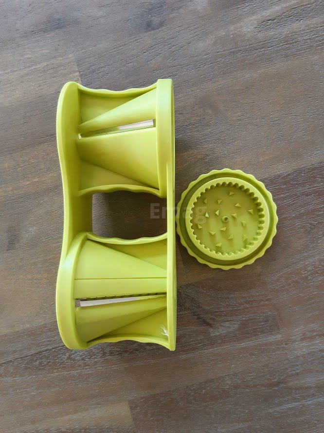 Groene groentespiraalsnijder met drie soorten messen, op een houten oppervlak.