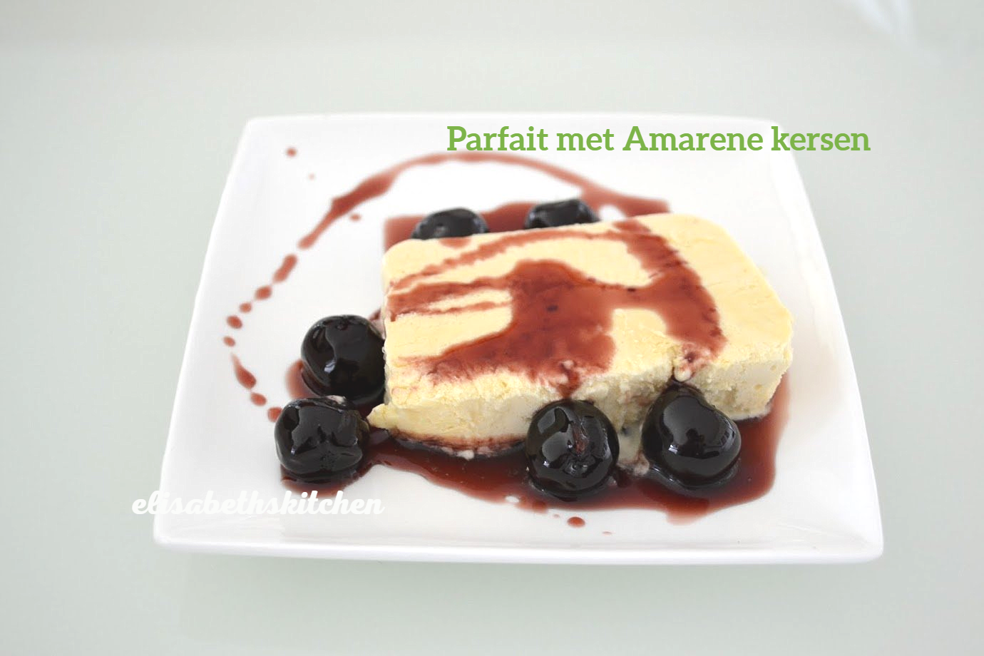 Parfait met Amarena-kersen op een wit bord, met kersen en saus.