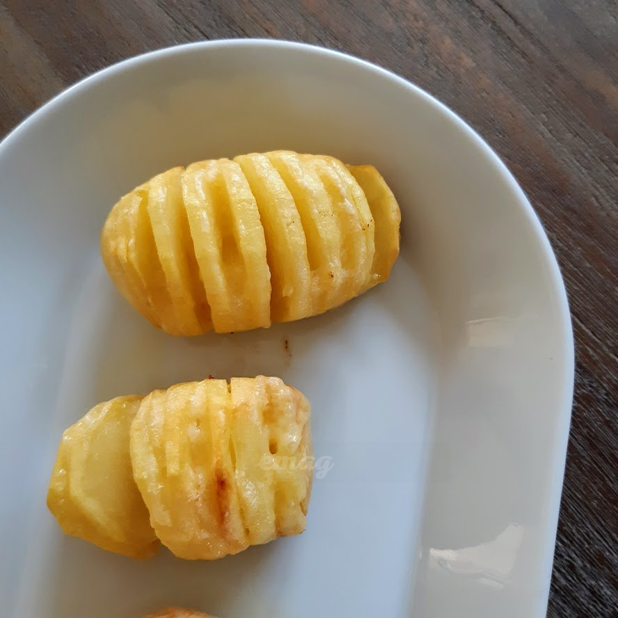 Hasselback-aardappelen op een wit bord, goudbruin en knapperig. Close-up op een houten ondergrond.