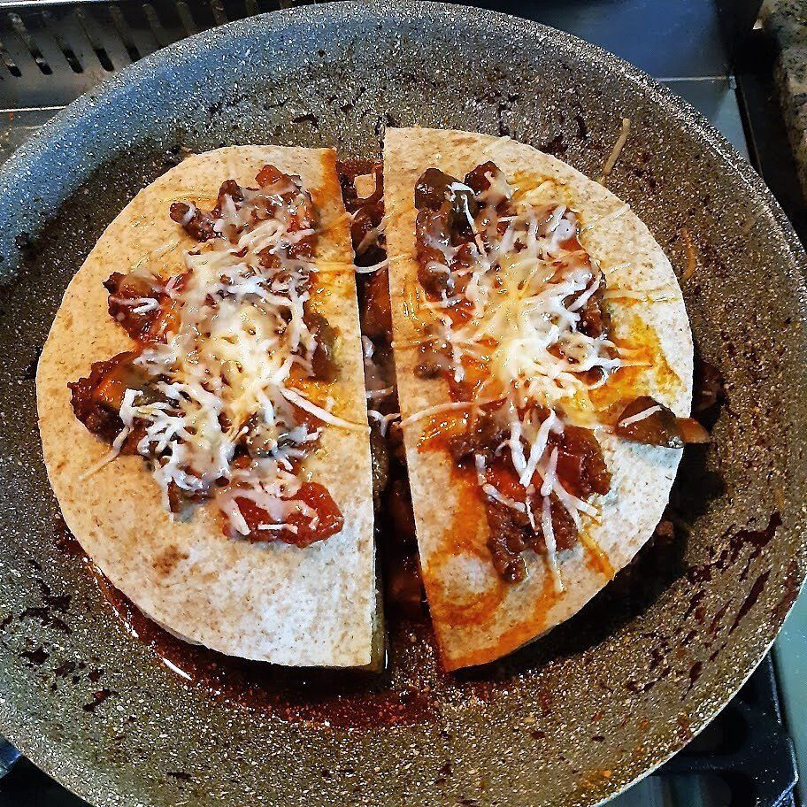 Een quesadilla die doormidden is gesneden en in een koekenpan is gebakken, gevuld met vlees, paprika en kaas.