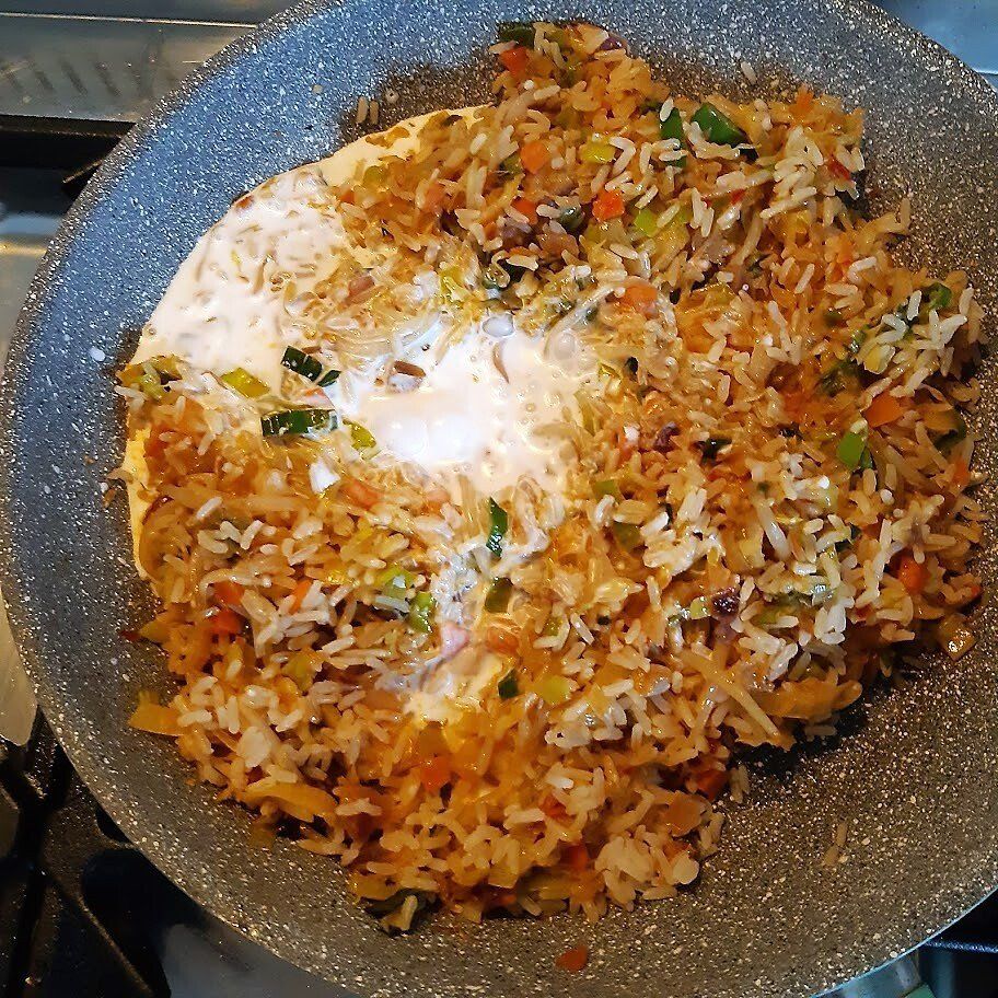 Gebakken rijst met een gebakken ei in een grijze pan. De rijst bevat zichtbare groene uitjes en oranje wortels.