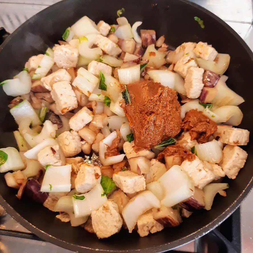 Tofu, uien en saus worden in een zwarte pan op het fornuis gekookt.