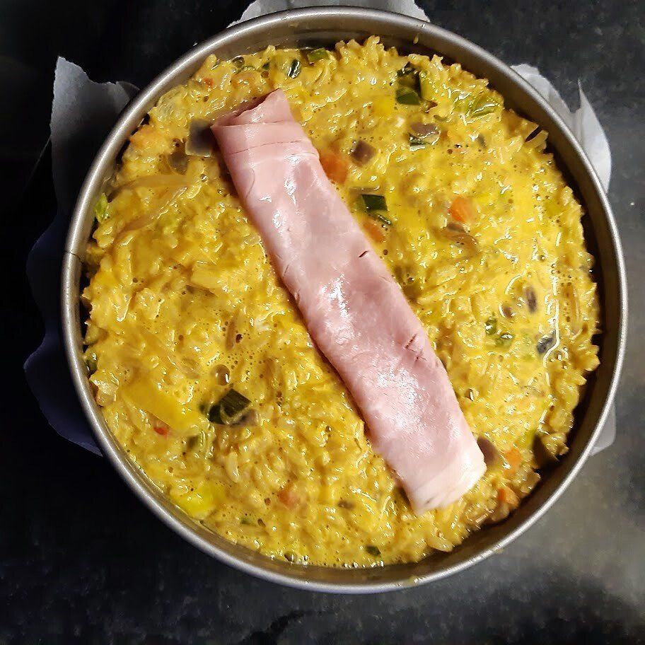 Een hartig rijstgerecht uit de oven in een ronde pan, gegarneerd met een plakje ham.