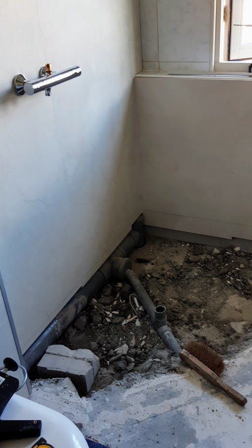 Badkamer in aanbouw met zichtbare leidingen en sanitair aan de muur.