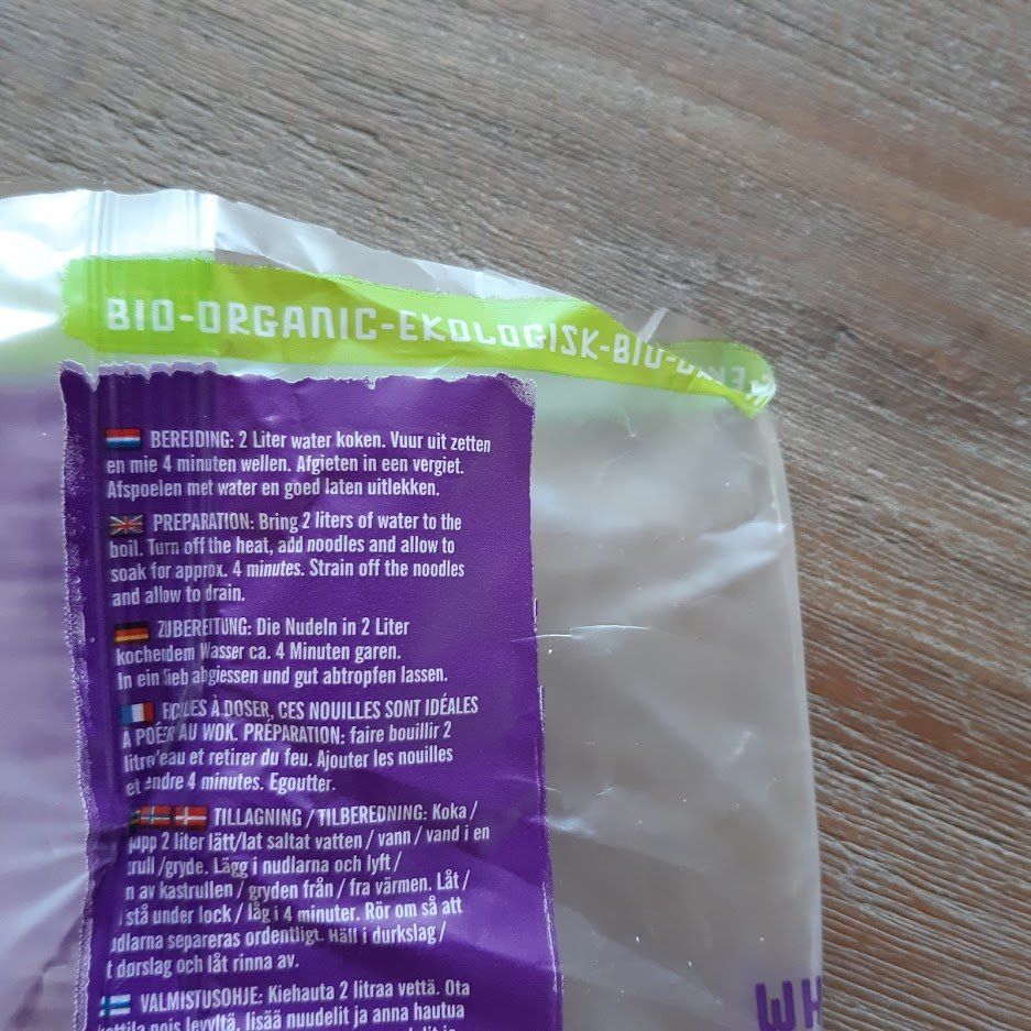 Close-up van een gedeeltelijk geopende plastic zak met voedsel, waarop paarse en groene tekst staat. Bovenaan staat 