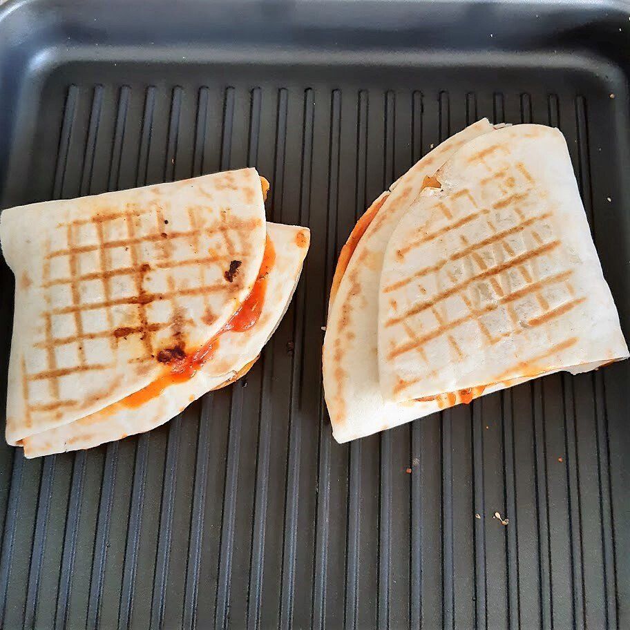 Twee quesadilla's op een grillpan, goudbruin met grillstrepen, gevuld met een sinaasappelvulling.