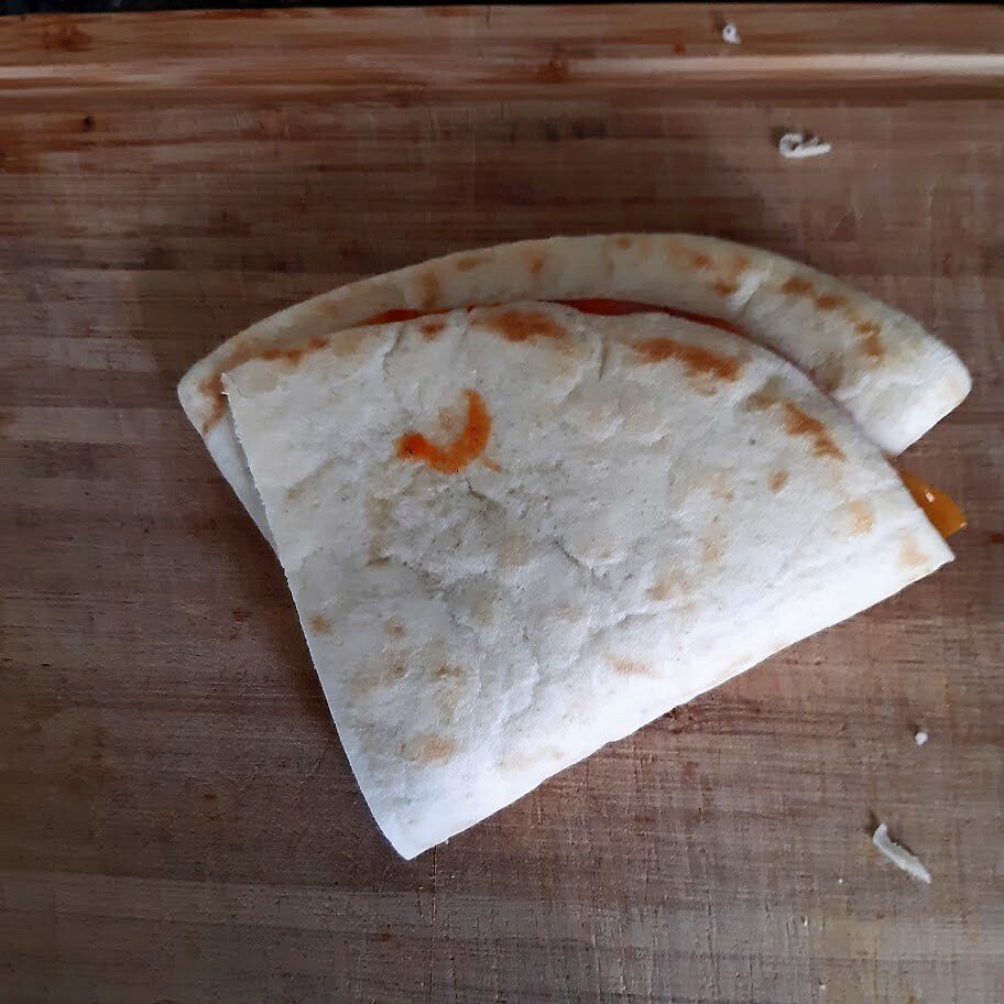 Quesadilla op een houten snijplank, dubbelgevouwen met een rode saus eronder zichtbaar.