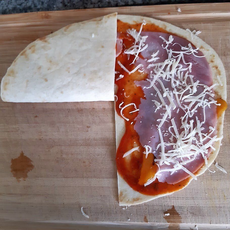 Een halve tortilla gevuld met ham, saus en kaas, dubbelgevouwen op een houten plank.