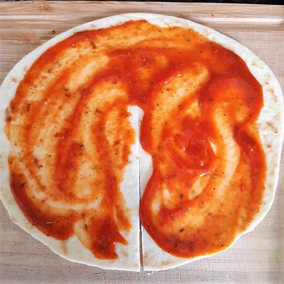 Een doormidden gesneden platbrood, bedekt met rode saus, op een houten plank.