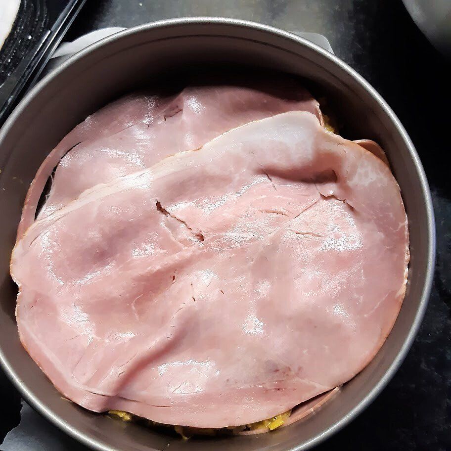 Plakjes ham worden in lagen in een ronde metalen pan gelegd, ter voorbereiding op een gerecht.