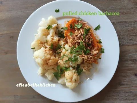 Pulled chicken barbacoa met bloemkool op een wit bord, gegarneerd met peterselie.