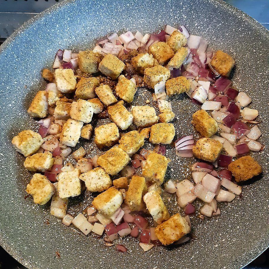 Croutons en in blokjes gesneden rode uien worden gebakken in een grijze pan.
