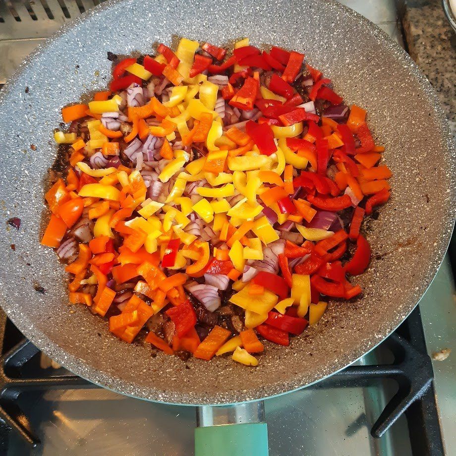 Kleurrijk gesneden paprika's en ui worden in een pan op het fornuis gebakken.