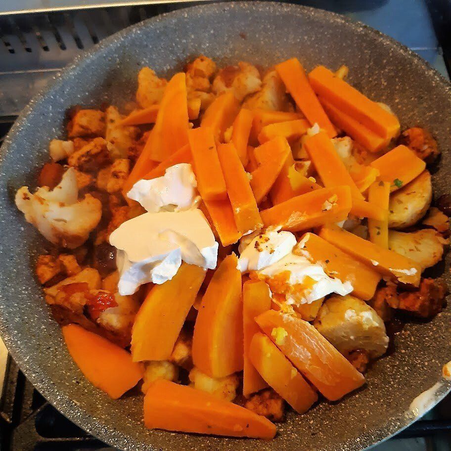 Een pan met groenten en tofu die aan het koken is, samen met wortelen, bloemkool en room.