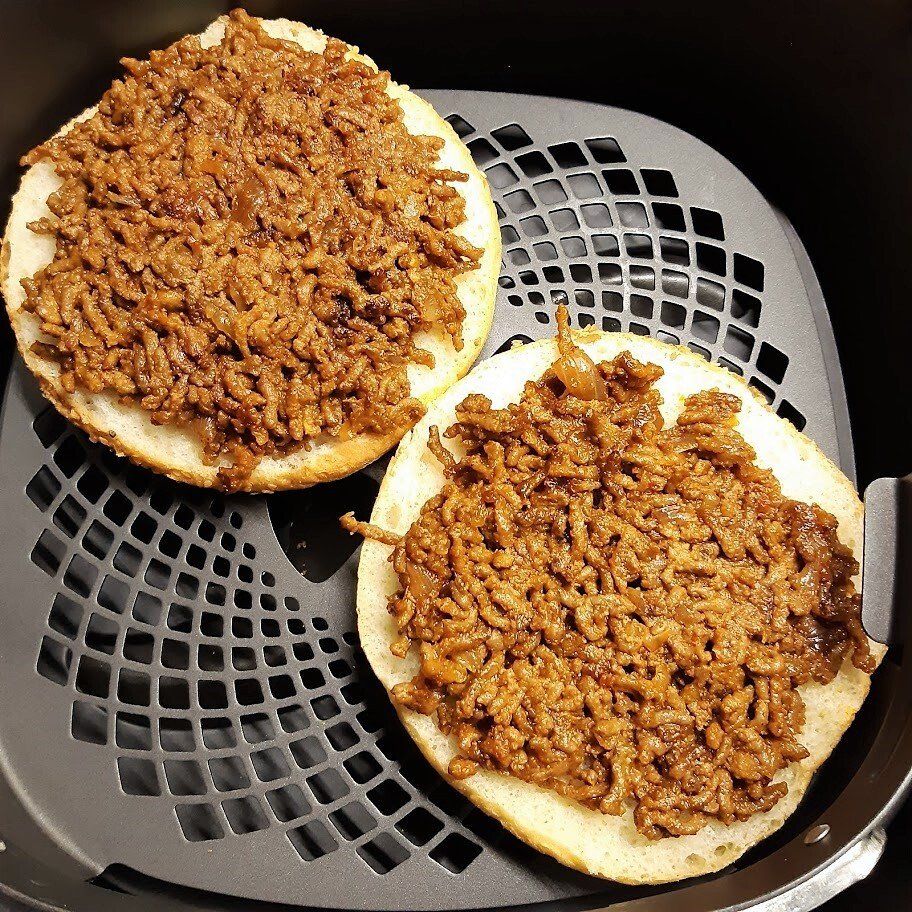 Twee hamburgerbroodjes gevuld met gekruid gehakt in een mandje van de airfryer.