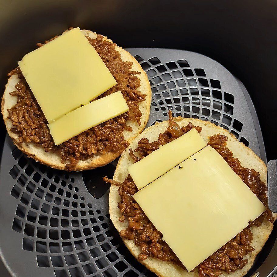 Twee open sloppy joe sandwiches met kaas in een mandje van de airfryer.