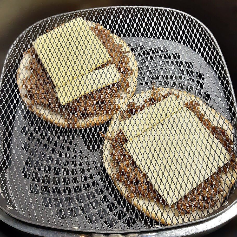 Twee minipizza's met reepjes vlees en plakjes kaas in een mandje van de airfryer.
