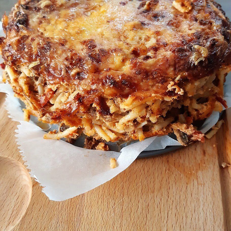 Gebakken pastataart met een goudbruine korst, hoog opgestapeld op bakpapier en een houten snijplank.