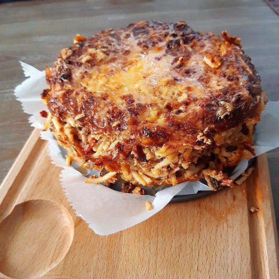 Ronde, goudbruine aardappelkoek op een houten plank, met een houten lepel ernaast.