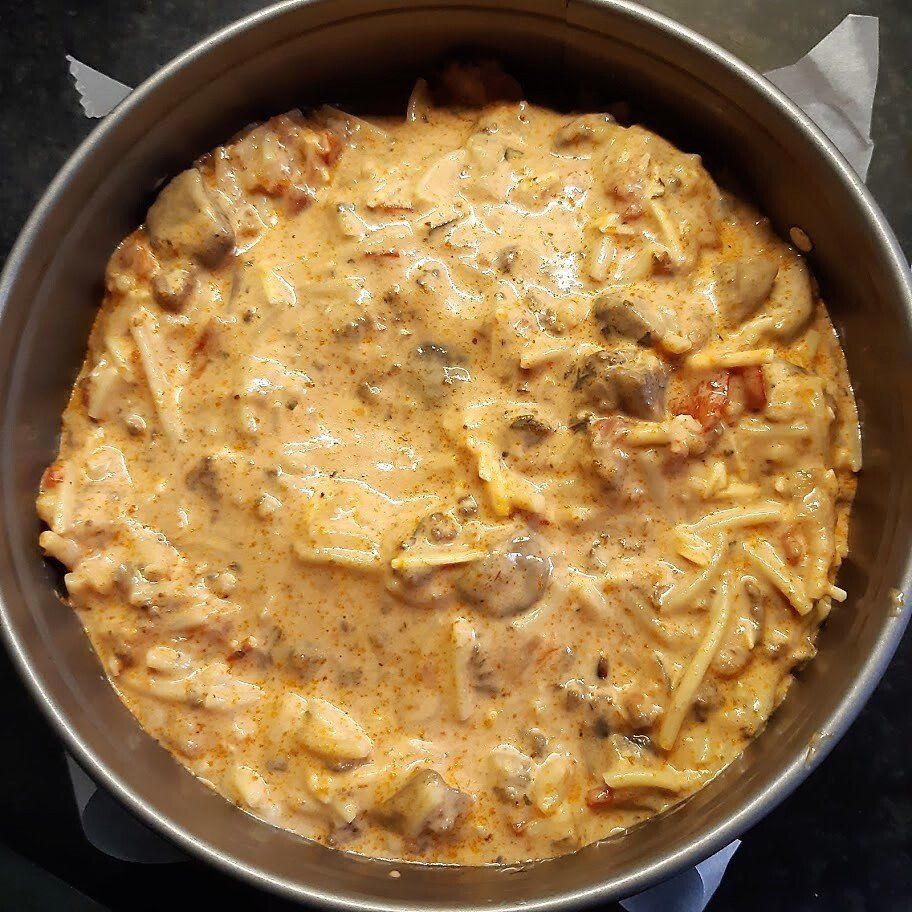 Romige pastaschotel in een ronde ovenschaal; sinaasappelsaus, champignons en kaas zichtbaar.