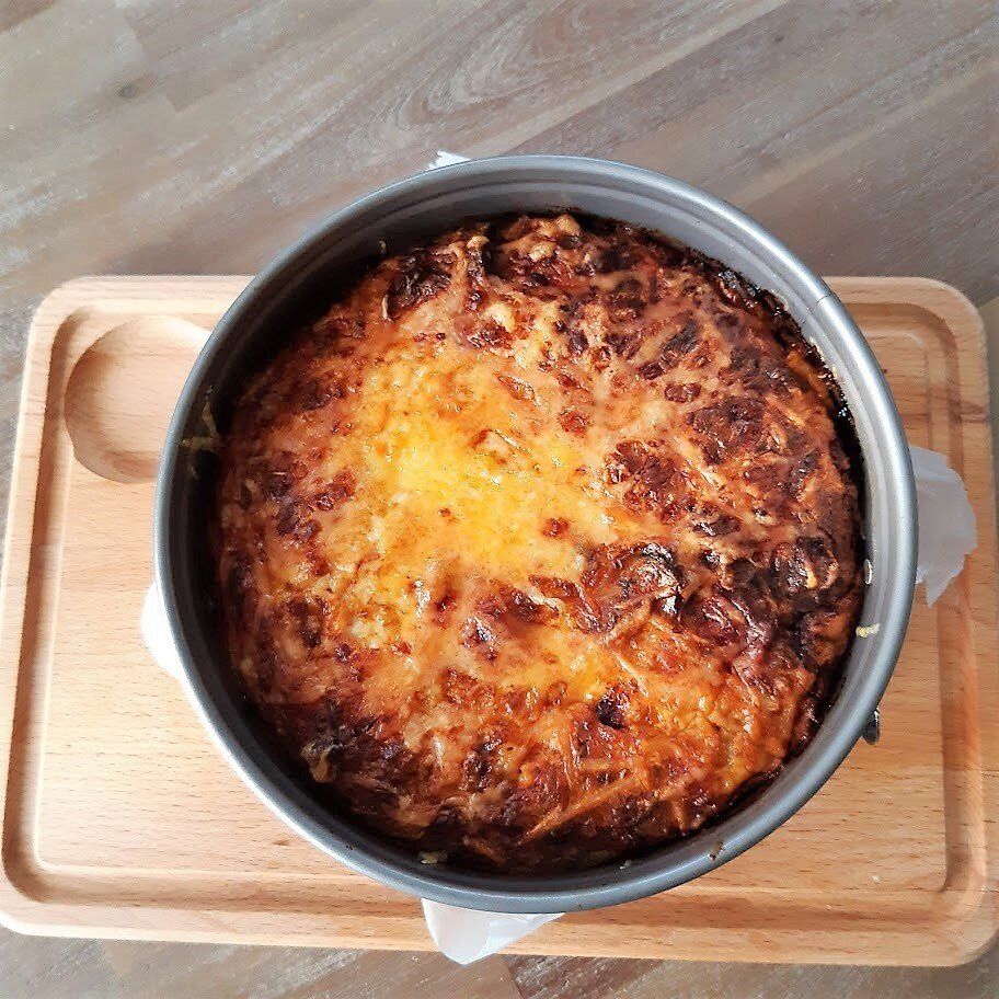 Gebakken, goudbruine quiche in een metalen springvorm op een houten dienblad.