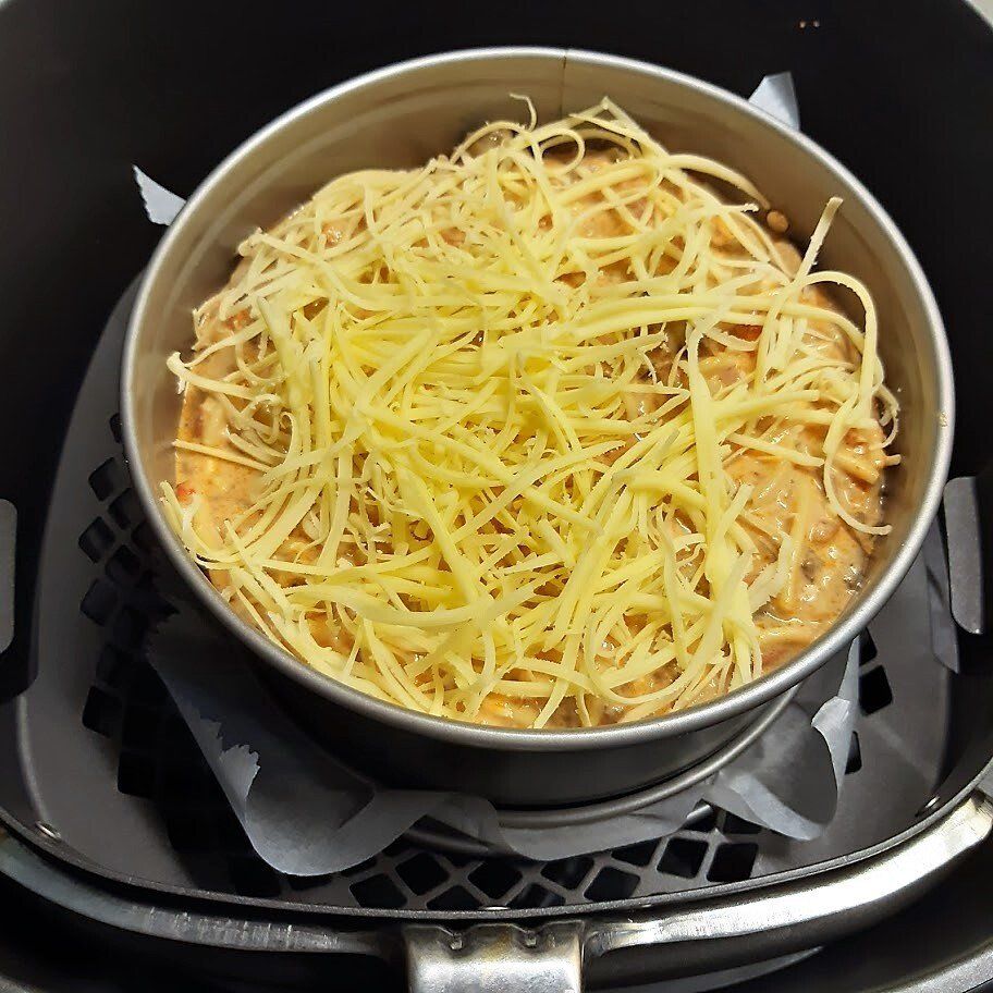 Ovenschotel met geraspte kaas in een ronde ovenschaal, geplaatst in een mandje van de airfryer.