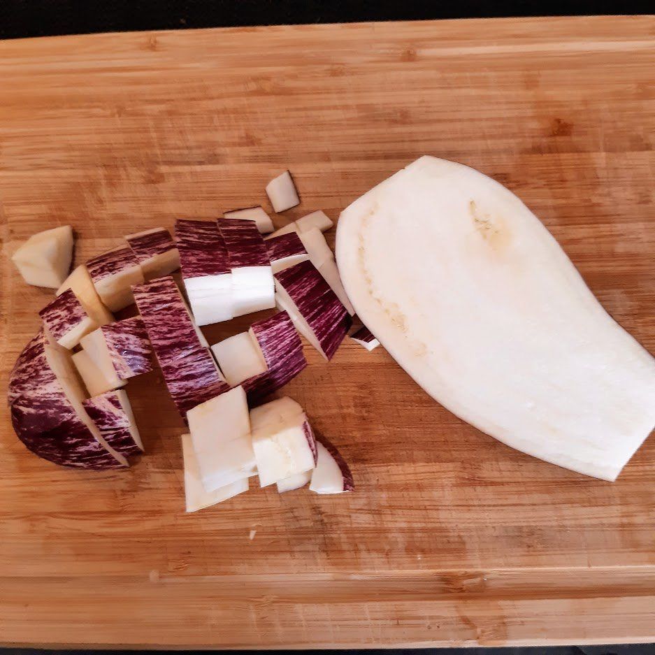 Gesneden aubergine op een houten snijplank; sommige stukken zijn in blokjes gesneden, een grote plak rechts.