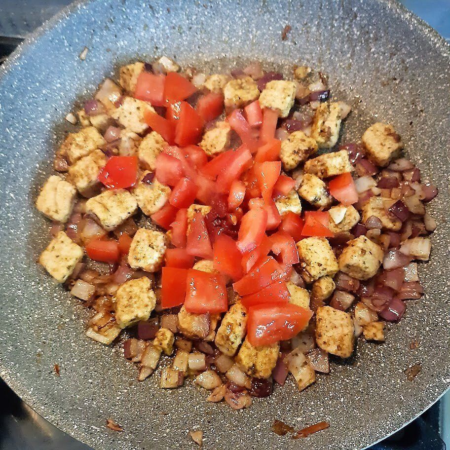 Een pan met gekookte kip, rode ui en in blokjes gesneden tomaten.
