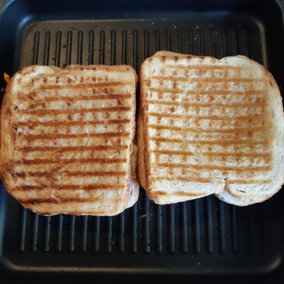 Twee gegrilde kaassandwiches op een grillpan, beide met grillstrepen, goudbruin.