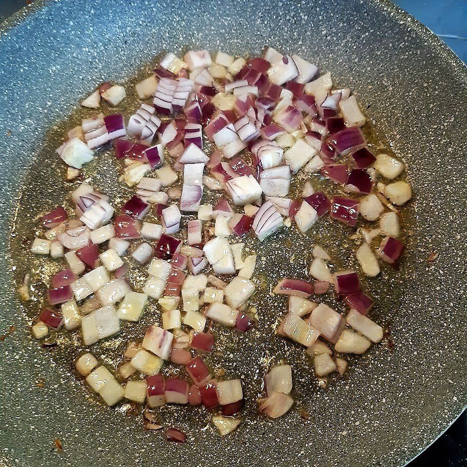 Gesneden rode uien en knoflook worden in een pan met olie gebakken.