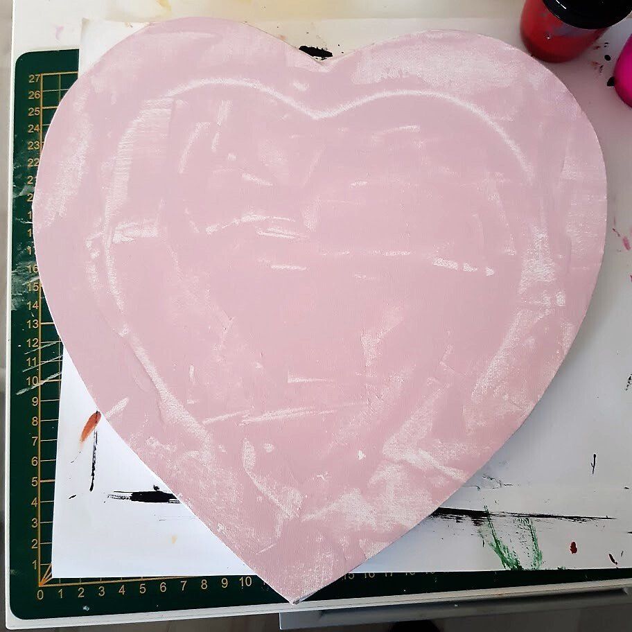 Roze, hartvormig houten plankje, gedeeltelijk beschilderd met witte strepen op een witte ondergrond.
